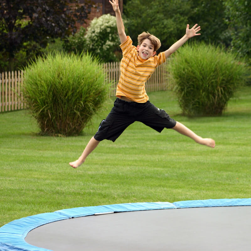 Ein Junge springt mit ausgestreckten Armen und Beinen in die Luft auf einem Trimilin Gartentrampolin